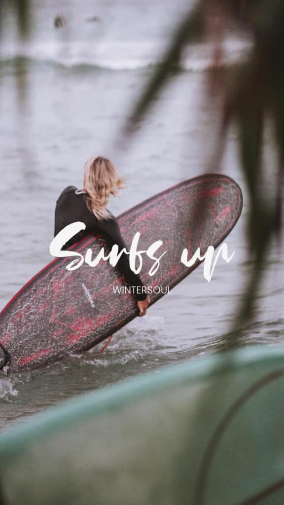 shows the words 'surfs up' Wintersoul - a bold boho script font with a photo of a blonde woman carrying a surf board into the sea