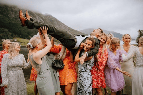 brightly dressed bridesmaids lifting bridegroom over their heads laughing against dramatic mountain backdrop