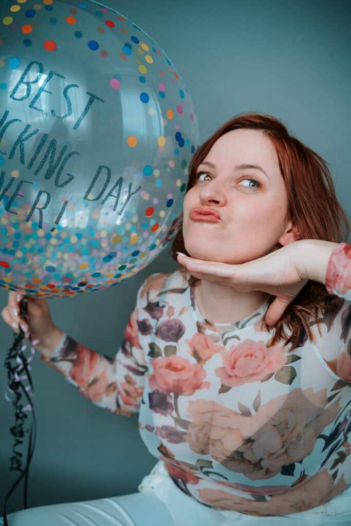 Photo of brand photographer, Inese, pulling a silly face, holding a confetti balloon that says best f**king day ever!